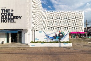 Das Core Gallery Hotel mit einer markanten, geometrischen Fassade und einem großen Wandgemälde einer Person in einer Hängematte.