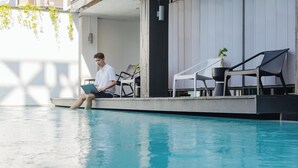 A poolside area with a person using a laptop, lounge chairs, and potted plants. - The Core Gallery Hotel (Chiang Mai)