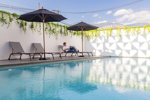 Ein Poolbereich mit Liegestühlen und Sonnenschirmen, eine Person entspannt und eine Bergblick im Hintergrund.