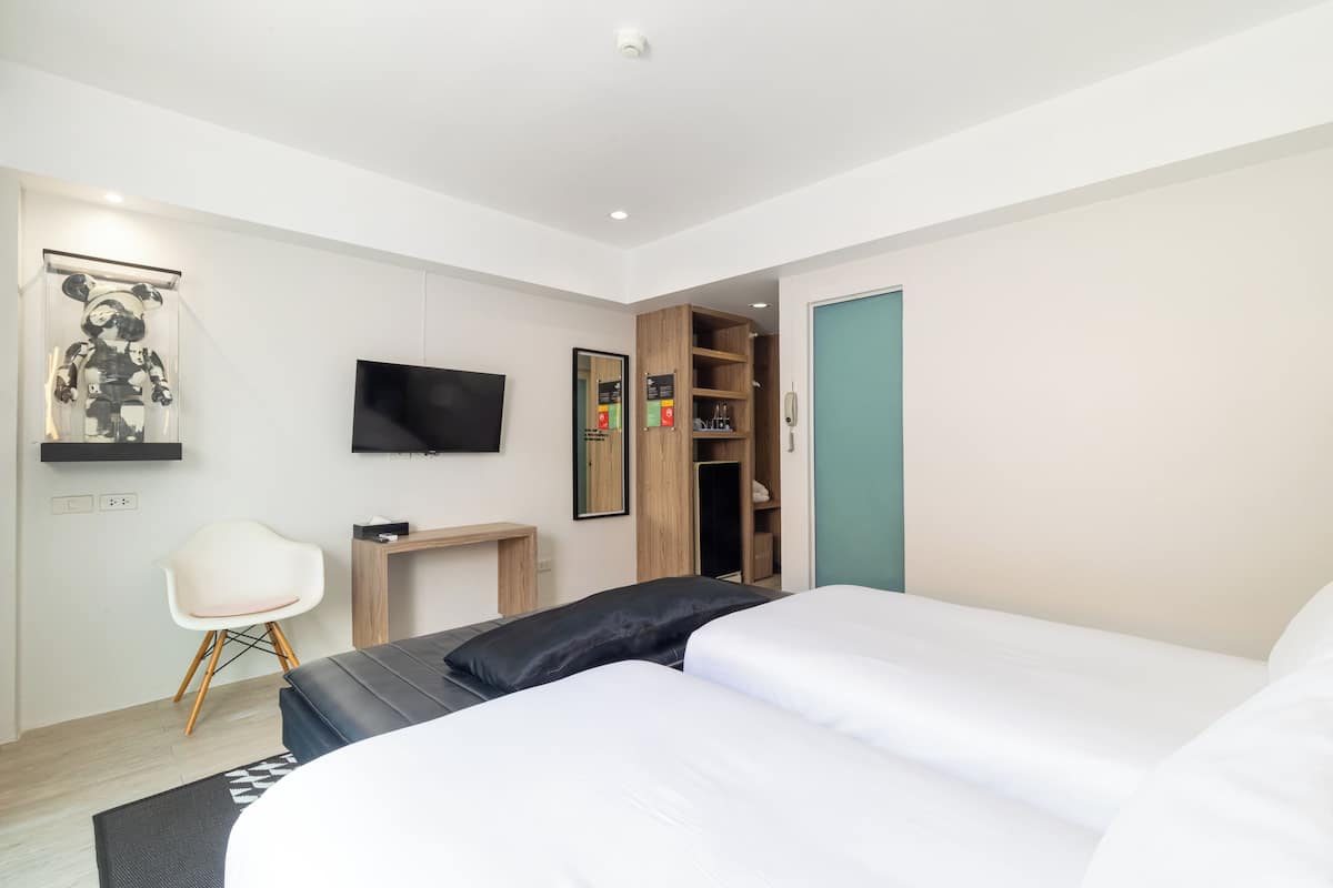 A modern hotel room with a bed, a desk, a chair, a TV, and a wardrobe.