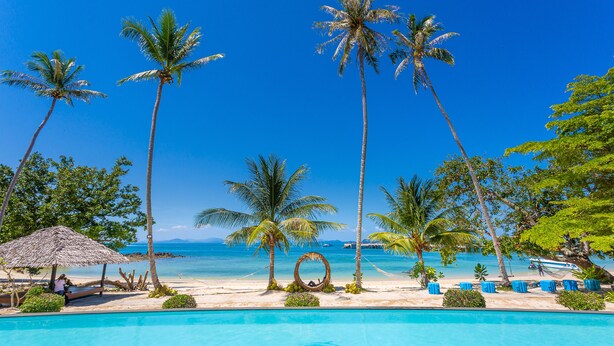 Ein tropisches Resort mit Swimmingpool, Palmen und einem Strand.
