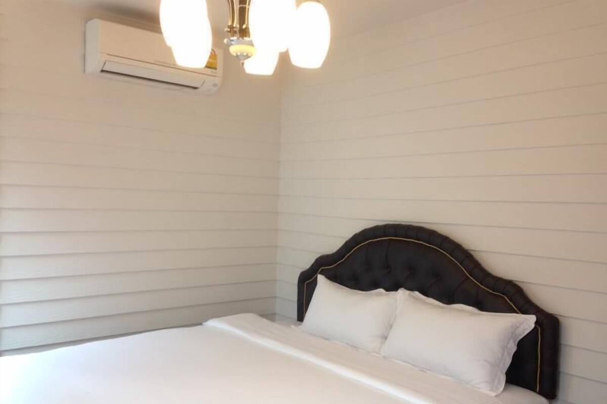 A neatly made bed with white linens and a dark headboard in a room with white paneled walls.