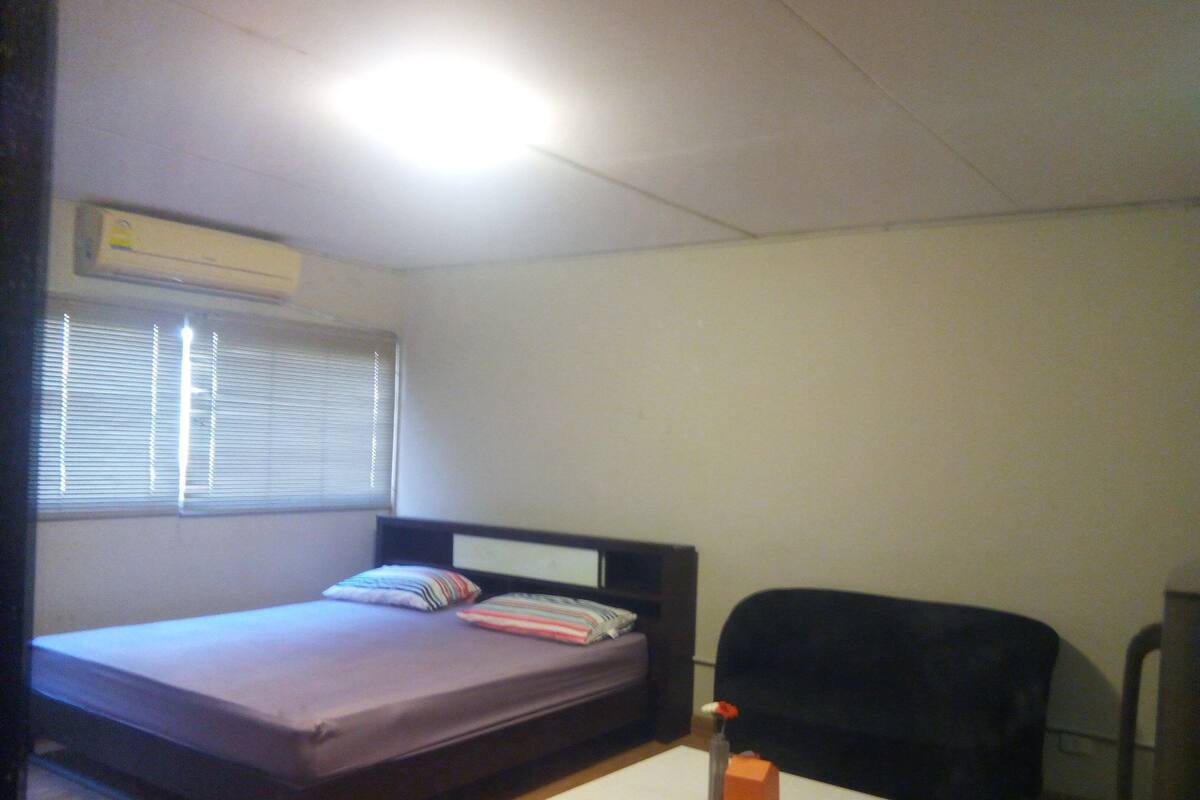 Ein kleiner, einfach eingerichteter Raum mit einem Bett, einem Sessel und einem kleinen Tisch.