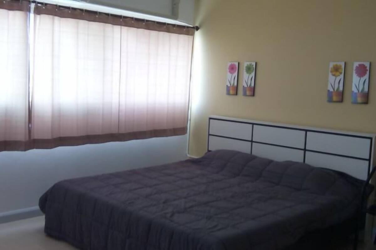 Ein Schlafzimmer mit einem Bett, einem Fenster mit Vorhängen und Wandbildern.