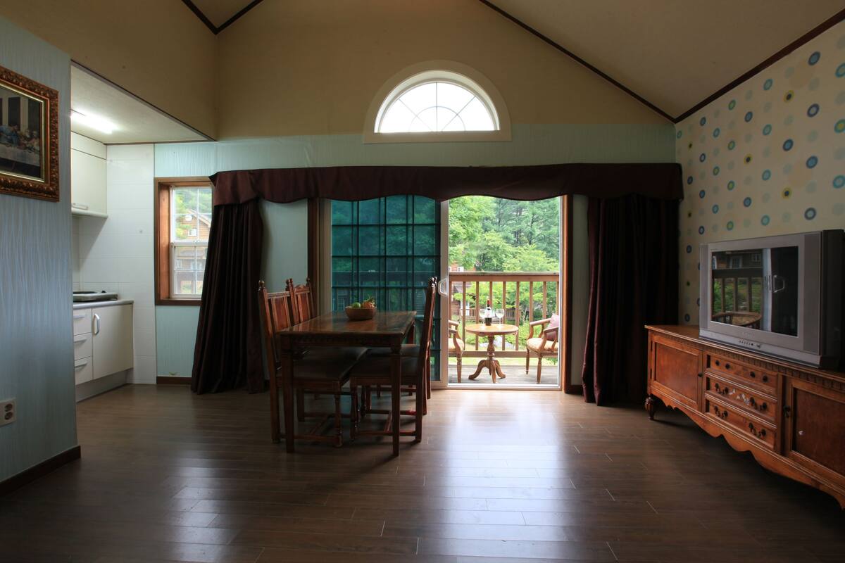 A dining area with a wooden table and chairs, a window with curtains, and a view of the outdoors.