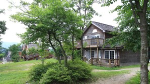 A wooden cabin with a balcony, surrounded by trees and a grassy yard. - Mayfair Pension (Pyeongchang)