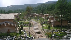 A rustic wooden cabin area with a stone pathway leading through it, surrounded by trees and hills. - Mayfair Pension (Pyeongchang)