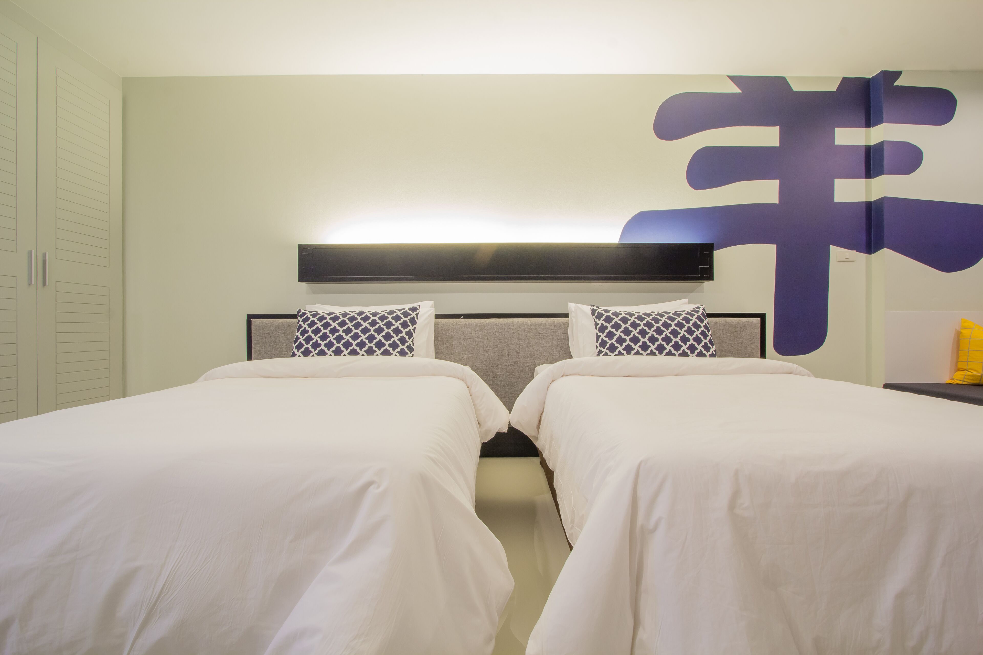 Ein Hotelzimmer mit zwei Betten, einer großen Wanddekoration und einem Fernseher, der über den Betten angebracht ist.
