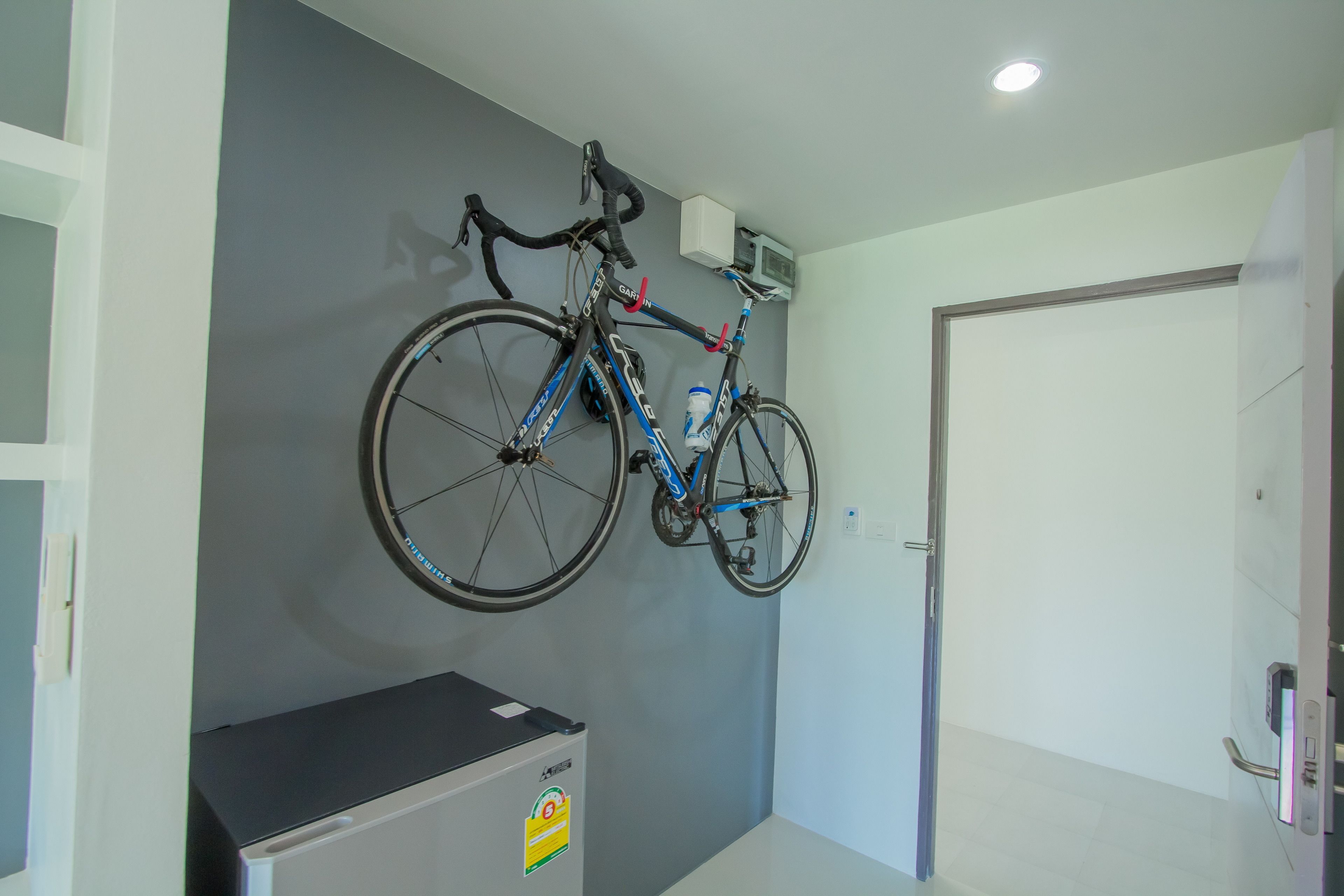 A room with a bicycle mounted on the wall, a small refrigerator, and a door.