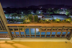 Un balcón con vistas a una piscina, rodeado de plantas en macetas y una barandilla.