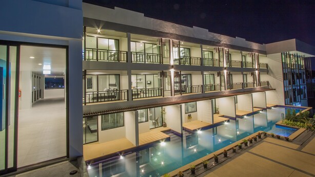 Un hotel moderno con piscina en la azotea, varios balcones y un interior bien iluminado.