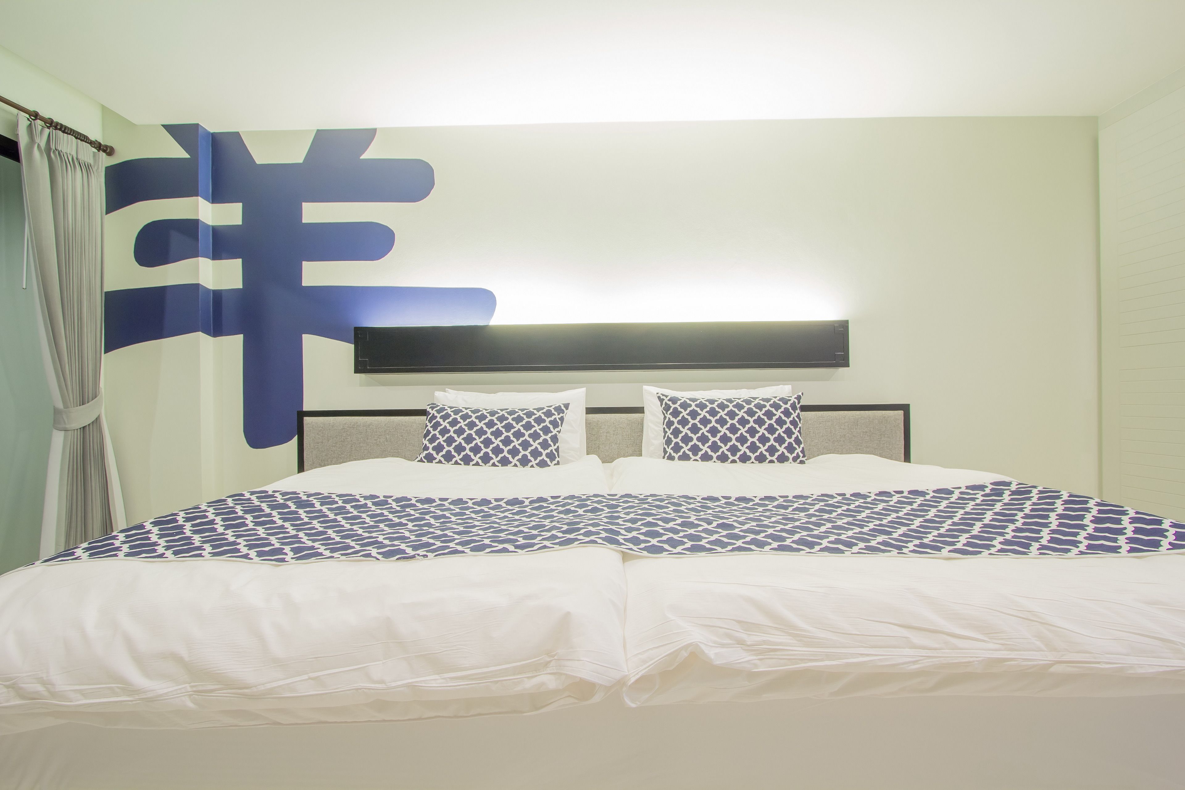 A hotel room with a large bed, a headboard with a light fixture, and a wall with a large decorative pattern.