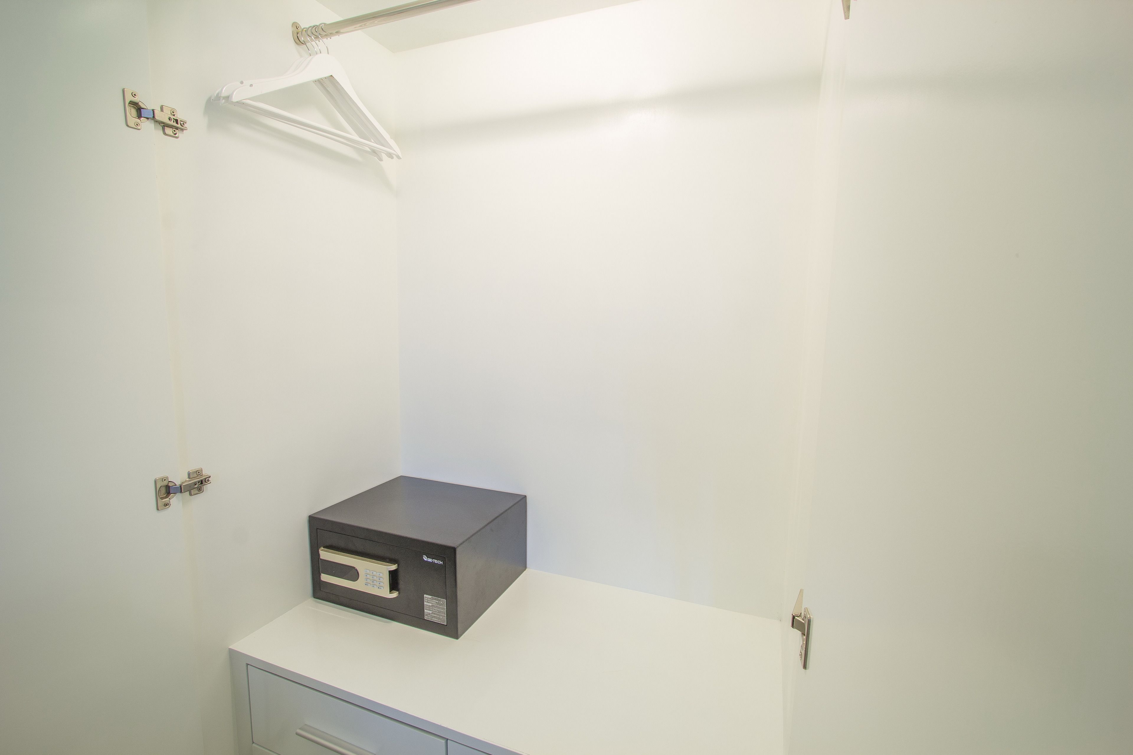 A small, white room with a single black device on a white counter, a door with a handle, and a light fixture above the door.