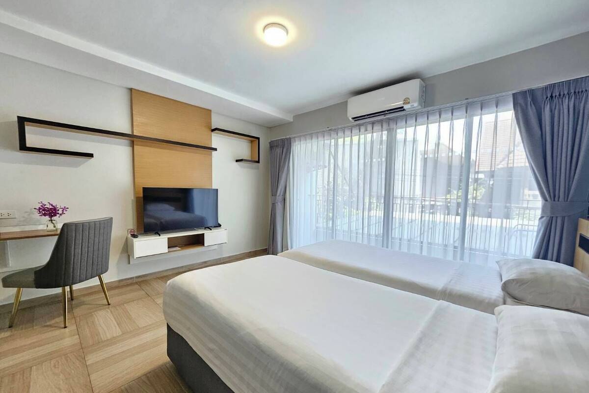 Ein Hotelzimmer mit zwei Betten, einem Schreibtisch mit Stuhl, einem Fernseher und einer Klimaanlage.