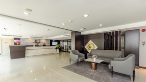 A modern lobby with a reception desk, grey sofas, a coffee table, and a decorative wall piece. - Chiva Bangkok Hotel (Bangkok)