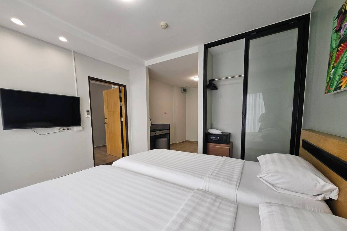 Ein Hotelzimmer mit einem großen Bett, einem an der Wand montierten Fernseher, einem Kleiderschrank und einem Duschbereich.