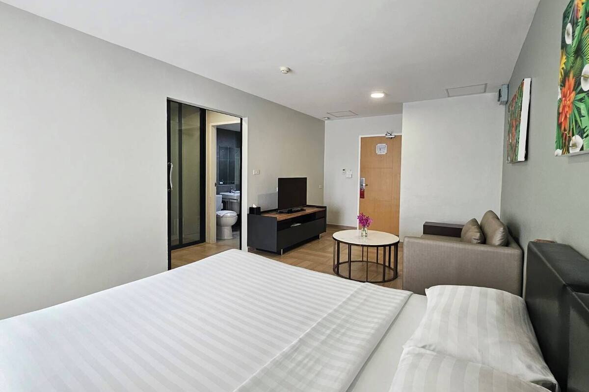 Ein Hotelzimmer mit einem großen Bett, einem Sofa, einem kleinen runden Tisch mit einer Vase und einem Fernseher.