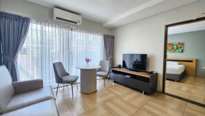 A modern hotel room with a sofa, a TV, a small table with a vase, and a bed with a headboard. - Chiva Bangkok Hotel (Bangkok)