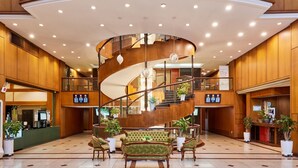 Eine geräumige Lobby mit einer zentralen Wendeltreppe, einem Empfangsbereich und zahlreichen Blumentöpfen.