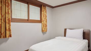 Uma cama de solteiro com cabeceira de madeira em um quarto com paredes brancas e uma janela com moldura de madeira.