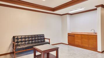 Una habitación con sofá de cuero negro, una mesa de centro de madera, un mueble de madera con lavamanos y un techo con vigas de madera e iluminación empotrada.