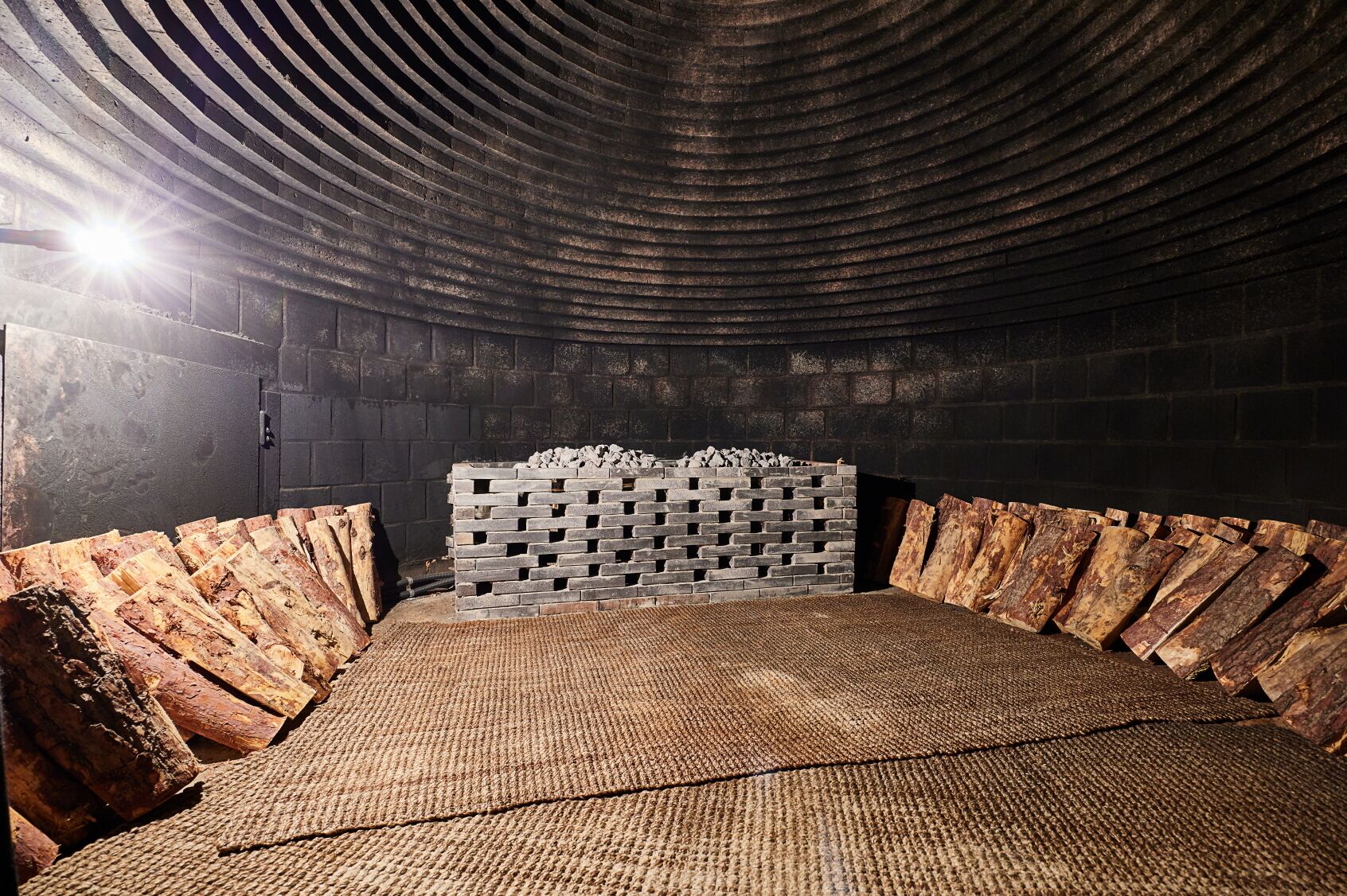 A room with a curved ceiling, a stack of firewood, and a woven floor mat.