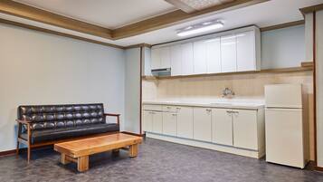 A compact kitchen with white cabinets, a wooden bench, and a refrigerator.