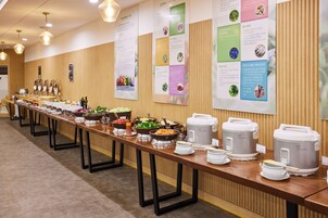 Montaje de bufé con varias estaciones de comida, incluyendo platos calientes y fríos, dispuesto sobre una mesa larga.