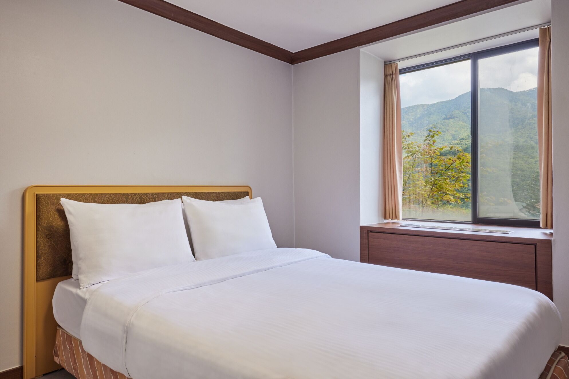Ein ordentlich bezogenes Bett in einem Zimmer mit großem Fenster und Blick auf die Berge.