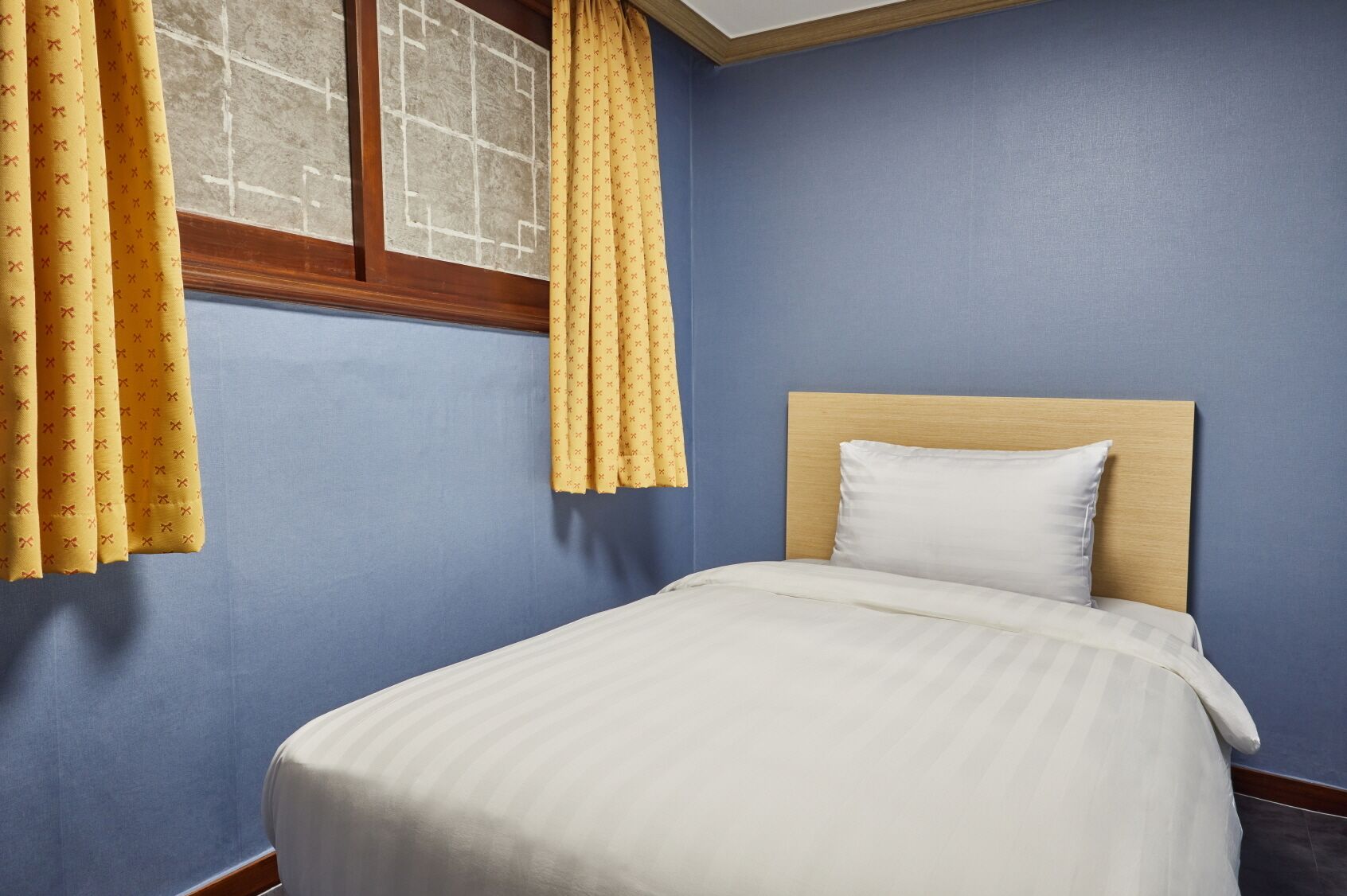 Ein Schlafzimmer mit einem Einzelbett, einem Holz-Kopfteil und gelben Vorhängen.