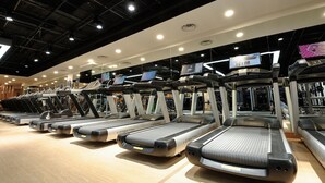 Eine Reihe von Laufbändern in einem Fitnessstudio mit Holzboden und Deckenbeleuchtung.