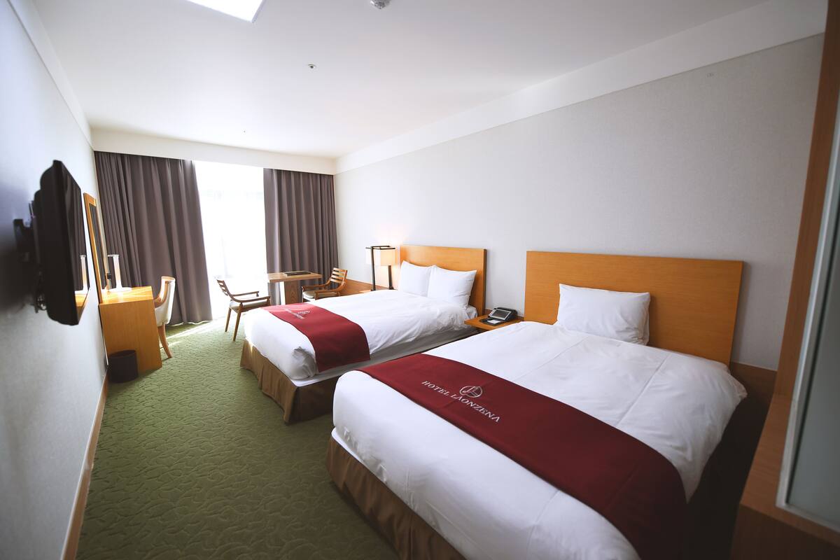 A hotel room with two beds, a desk, and a chair.