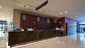Ein Hotelrezeptionstresen mit Marmorplatte, moderner Pendelleuchte und einem Schild, das den Weg zum Restaurant weist.