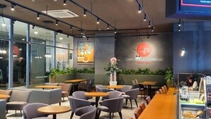 Ein modernes Café-Interieur mit Tischen, Stühlen, einer Theke und einer Wand mit Logo und Schriftzug.