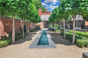 A courtyard with a central water feature, surrounded by brick walls and trees. - The Houston (Wagga Wagga)