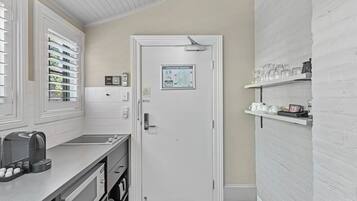 A modern kitchen with a white brick wall, a white door with an evacuation diagram, and shelves with kitchenware.