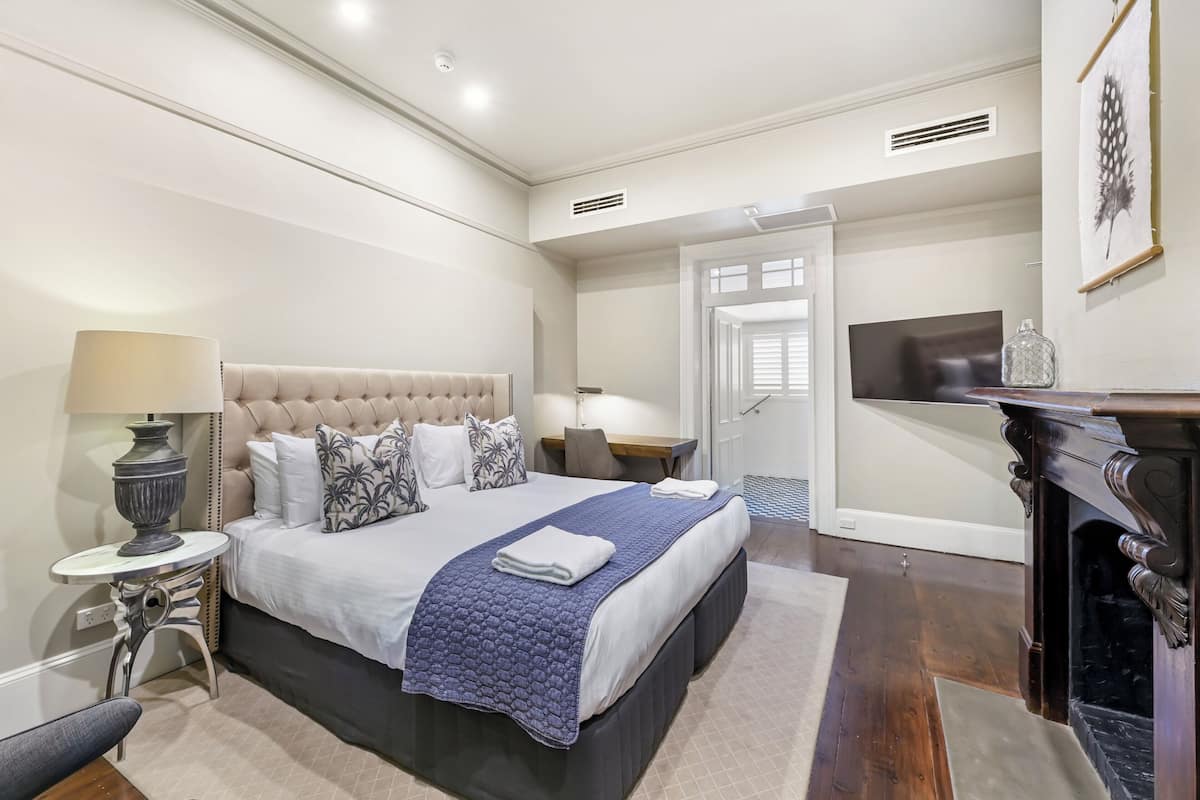 A modern bedroom with a large bed, bedside tables, a TV, and a fireplace.