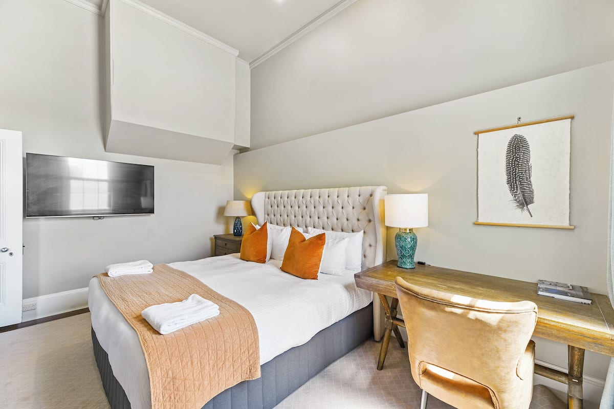 A hotel room with a bed, bedside table, lamp, chair, and artwork on the wall.