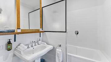 A bathroom with a white sink, mirror, and bathtub.