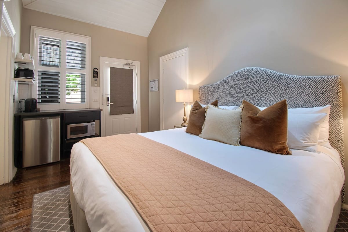 A hotel room with a large bed, a kitchenette, and a door leading to the outside.