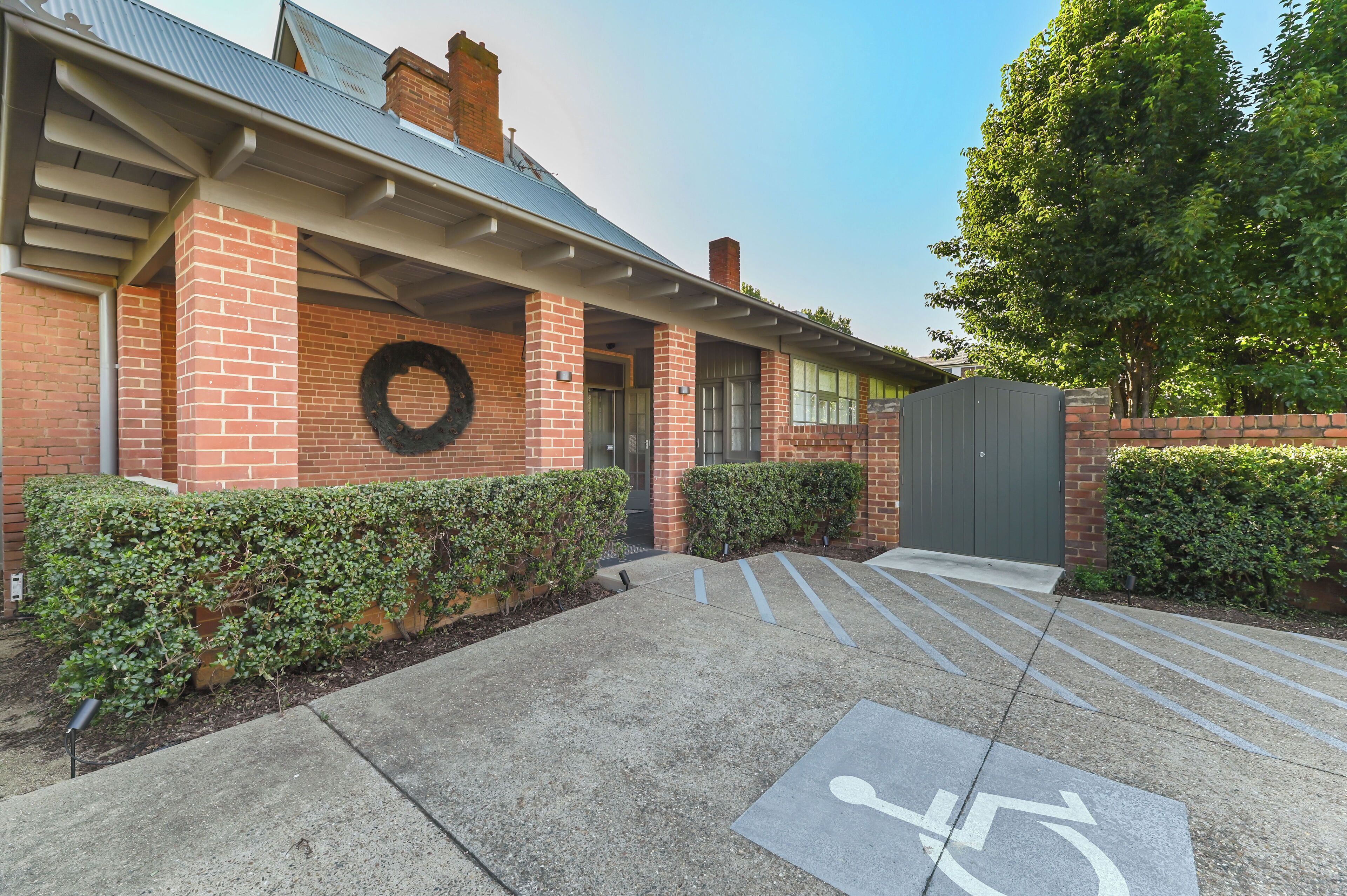 A brick building with a covered entrance, a wheelchair-accessible parking area, and a green tree in the background.