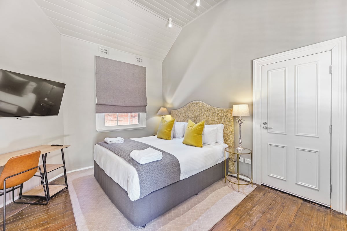 A bedroom with a bed, a desk, a chair, a TV, and a door.
