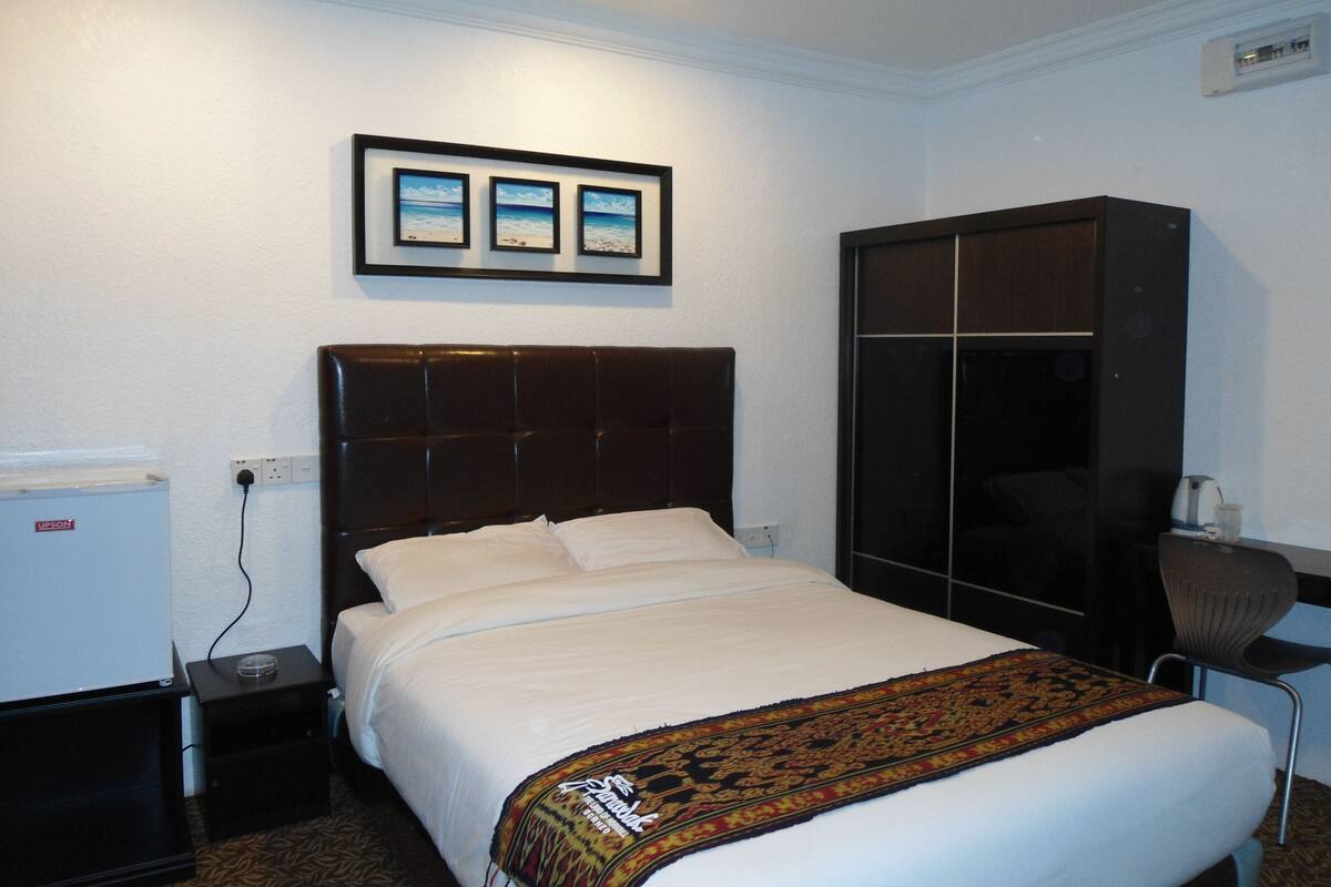 Una cama bien hecha con cabecera, una mesita de noche pequeña, un armario y un cuadro enmarcado en la pared.