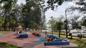 Un parque infantil con toboganes y estructuras para escalar, rodeado de árboles y vistas al agua.