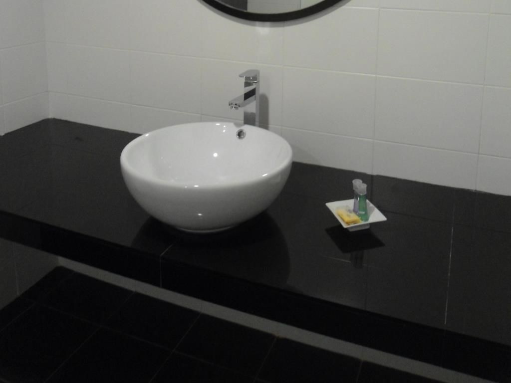 A bathroom with a white sink, black countertop, and a small bottle of hand soap.