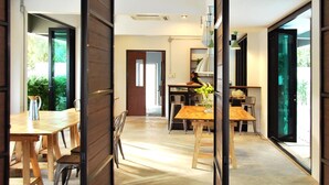 Un interior moderno con una mesa y sillas de madera, una zona de cocina con estufa y ventanas amplias que dejan entrar luz natural.