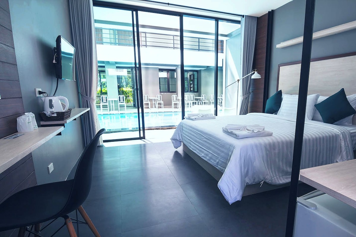 Une chambre d’hôtel moderne équipée d’un lit, d’un bureau et offrant une vue sur l’espace extérieur avec piscine.