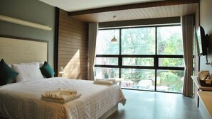 Un dormitorio amplio con una cama grande, un ventanal con vistas a zonas verdes y un televisor de pantalla plana montado en la pared.