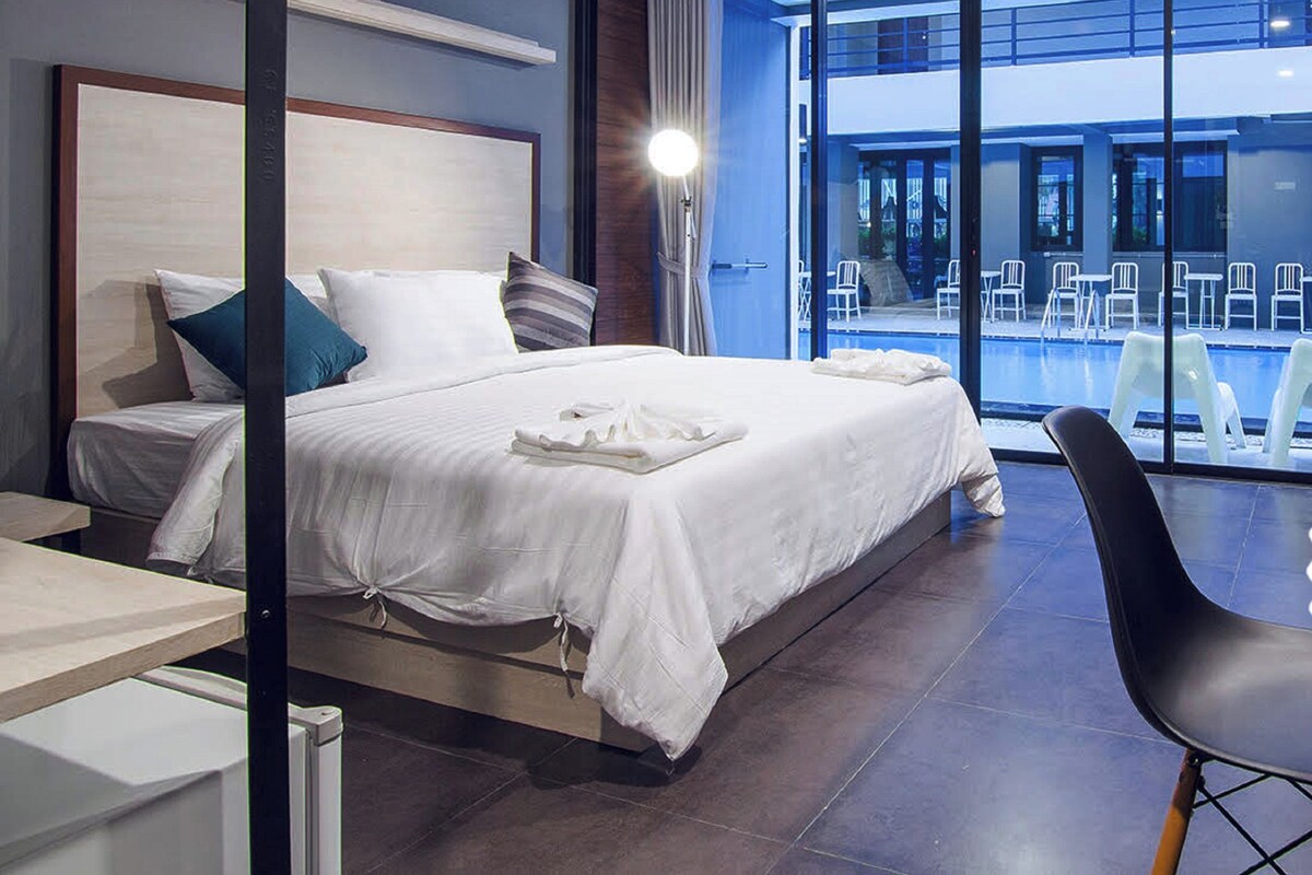 A hotel room with a large bed, a view of a swimming pool, and a sign indicating it is a Thailand Safety & Health Administration certified hotel.
