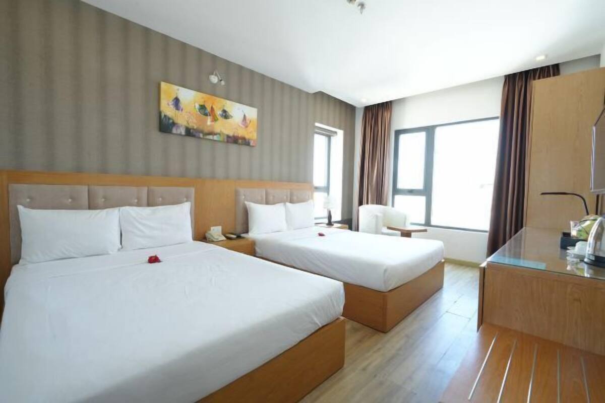 Habitación de hotel con dos camas, un escritorio, una silla, un cuadro en la pared y una ventana con cortinas.